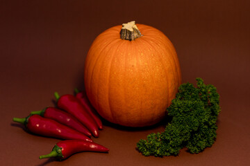 Pumpkin, chili peppers and parsley on brown background.Composition of vegetables