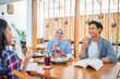 © Odua Images - three students eat snacks and drink and chat while working assignments at a cafe