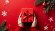© Kate Mayer - Woman's hands holding a gift box on a red background. Christmas gifts. Holiday mood. Flat lay, top view. Copy space
