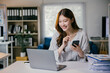 © PaeGAG - Smiling businesswoman using laptop and smartphone in a modern office, showcasing joy and positivity while managing tasks efficiently