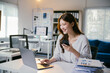 © PaeGAG - Smiling businesswoman is working on a laptop and using a smartphone at her desk in a modern office. She is surrounded by paperwork and digital devices