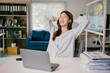© PaeGAG - Young businesswoman takes a moment to stretch and relax at her desk in a modern office, looking happy and stress-free