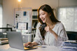 © PaeGAG - Young businesswoman happily shops online with a laptop and credit card at her office desk, showing satisfaction in managing finances digitally
