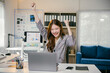 © PaeGAG - Young businesswoman is sitting at her desk and raising her arms in the air with excitement as she celebrates a big accomplishment at work