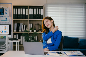 Young businesswoman is holding her neck in pain while sitting at her desk in the office. She is feeling the strain of working long hours on her computer