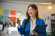 © PaeGAG - Young businesswoman is using colorful sticky notes on a glass wall to plan a project while holding a clipboard in her other hand