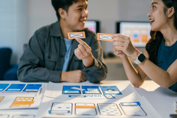 Poster - Two asian professionals collaborate on a mobile app, brainstorming ideas with icon cards in an office, discussing and planning with smiles. Their teamwork and creativity shine as they strategize ux