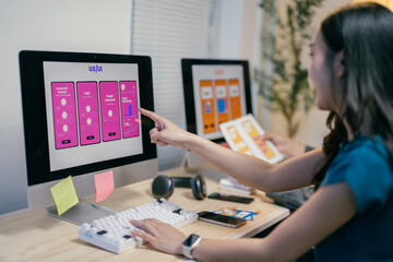 Poster - Two asian ui/ux designers are discussing the design of a mobile application interface displayed on a desktop computer, comparing it with sketches printed on paper