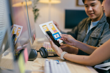 Poster - Two web designers are comparing a paper prototype with a mobile phone screen, discussing the layout and functionality of a new app