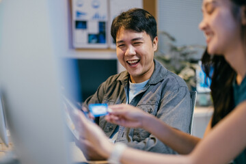 Poster - Two software developers are having fun while working together in the office. They are looking at a funny meme on a smartphone