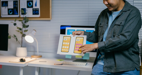 Poster - Asian ui designer is comparing two different versions of a mockup for a mobile phone app while working in his office