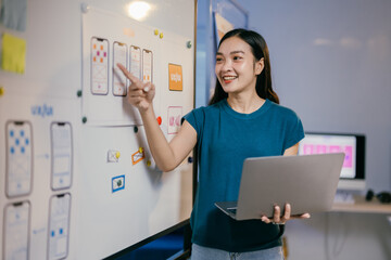 Poster - Ui ux designer is standing and pointing at a whiteboard with mobile application interface wireframes on it while holding a laptop