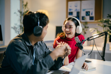 Two young radio hosts are recording a podcast, laughing and connecting with each other while wearing headphones in a professional studio