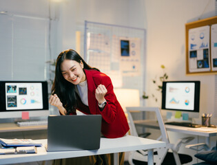 Poster - Young professional is raising her fists in the air, excited about the good news she received on her laptop while working late