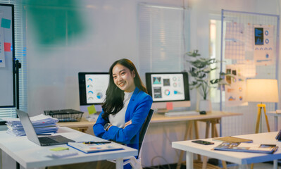 Poster - Young professional is working late in her office, surrounded by computers and paperwork, with a determined and focused expression on her face