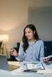 © Parichat - Businesswoman is working late and participating in a video conference call on her laptop, analyzing charts and taking notes