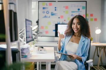 Poster - office worker is holding a tablet and gesturing thumbs up while sitting at her desk with graphs and 