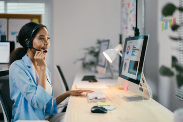 Poster - young professional woman is speaking into a headset while working late at the office. she is typing 