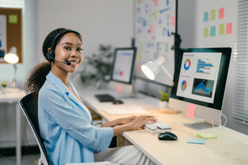 Fototapete - Young professional wearing a headset is working on her computer in her home office, surrounded by notes and office supplies