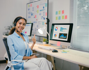 Poster - office worker is showing a thumbs up gesture while sitting at her desk in a modern office. she is we