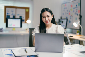 Aufkleber - Young asian businesswoman sitting at her desk and working on a laptop computer, she is smiling and appears to be happy with her work