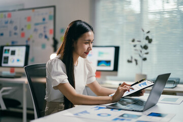 Poster - Young asian businesswoman works late in her office, analyzing financial data on her laptop with intense focus, showcasing her determination for success