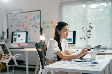 Poster - Businesswoman working with laptop computer and analyzing marketing information on a document with charts and graphs while sitting at her desk in the office
