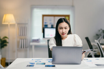 Poster - Businesswoman working at the office with a laptop computer and holding a clipboard with financial documents, she is analyzing business data on a laptop