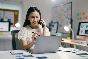 young asian businesswoman works late in a modern office, smiling while on the phone and laptop, show