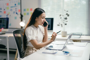 Poster - Young businesswoman is working in her bright modern office, having a phone call while analyzing financial data on her laptop
