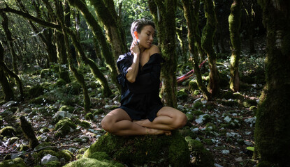 A pretty yoga girl meditates in a magical forest among moss-covered trees