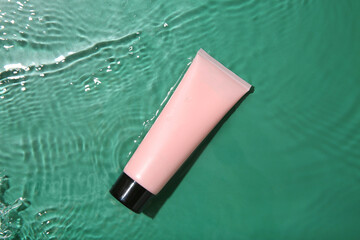 Poster - Cosmetic product. Tube with cream in water on green background, top view