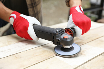 Poster - Man polishing wooden planks with angle grinder outdoors, closeup