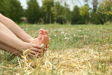 Canvas Print - Woman sitting barefoot on straw outdoors, closeup. Space for text