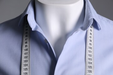 Male mannequin with light blue shirt and measuring tape on grey background, closeup