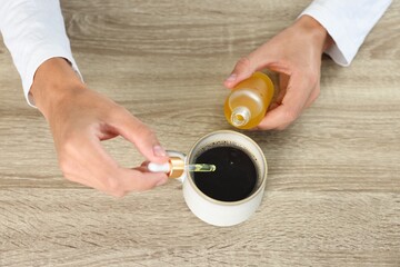 Poster - Young man dripping CBD tincture into drink at wooden table, above view