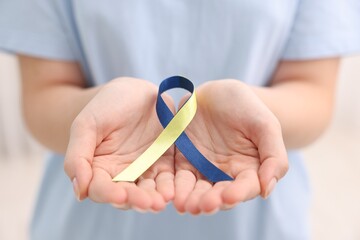 Poster - Woman with yellow and blue ribbon on light background, closeup. Down syndrome awareness