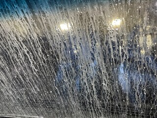 Soap and water splashing on a car windshield during a late evening car wash under bright lights