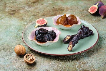 Wall Mural - Set of Georgian cuisine sweets. Fig jam, churchkhela and green walnut jam in pink bowls on a green plate on a green concrete background