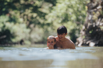 Wall Mural - Two happy friends swimming in a natural, tranquil lake surrounded by lush greenery, enjoying a sunny day and the refreshing water.