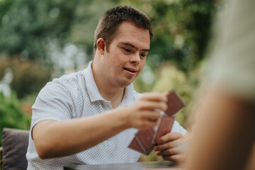 A young man with Down syndrome enjoying a card game outside in a relaxed setting, showcasing inclusion and friendship.