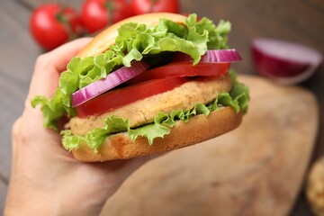 Woman holding vegetarian burger with chickpea cutlet at table, closeup