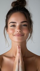 Spiritual Young woman with natural skin and her hair tied in a bun is holding her hands together in front of her chest and smiling serenely; clasping hands for prayer and namaste gesture