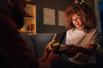 Young woman opening christmas gift with boyfriend on couch