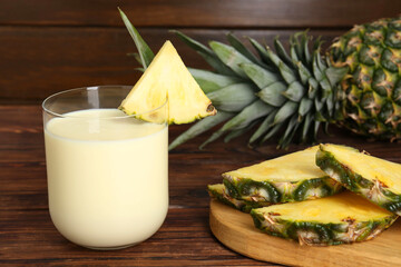 Tasty pineapple smoothie in glass and slices of fruit on wooden table, closeup