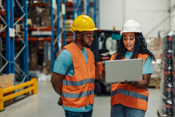 Wall Mural - Warehouse workers using laptop discussing logistics and inventory management