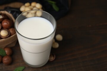 Poster - Glass of macadamia milk and nuts on wooden table, closeup. Space for text