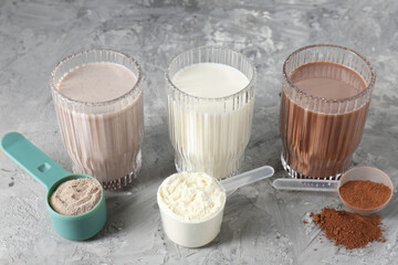 Poster - Delicious protein shakes in glasses and scoops with powder on gray textured table, closeup