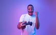 © Prostock-studio - Video Gaming Concept. Euphoric African American Guy With Joystick Celebrating Game Win, Cheerful Black Man Raising Fist And Exclaiming With Excitement, Standing In Neon Light Over Purple Background