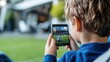 © Pinklife - A young child captures an image of a soccer ball with a smartphone, showcasing modern technology and a passion for sports in a stadium setting.